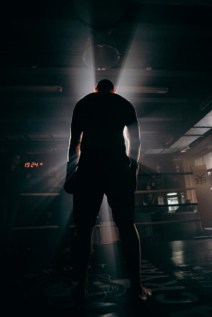 Silhouette of a boxer in a gym, illuminated by dramatic beams of sunlight, creating a powerful visual impact.